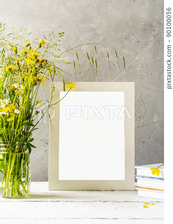 Mock up creation. White frame on white wooden table with grey concrete background and wild spring flowers 90100056