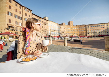Woman having breakfast at outdoor cafe with beautiful view on main square of Siena city, Italy Woman having breakfast at outdoor cafe with beautiful view on main square of Siena city, Italy 90100747