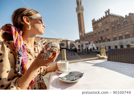 Woman having breakfast at outdoor cafe with beautiful view on main square of Siena city, Italy Woman having breakfast at outdoor cafe with beautiful view on main square of Siena city, Italy 90100749