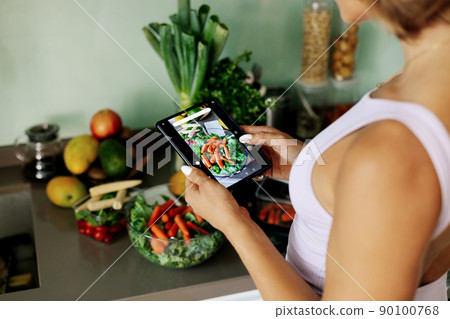 Close-up of a girl's hand taking a photo on her phone. A young woman, a culinary blogger, cooks in her home kitchen and takes photos on her smartphone. 90100768