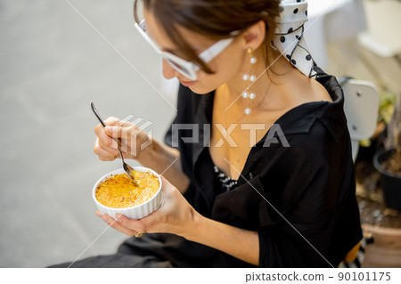 Woman eating dessert with creme brulee at the restaurant outdoors Woman eating dessert with creme brulee at the restaurant outdoors 90101175
