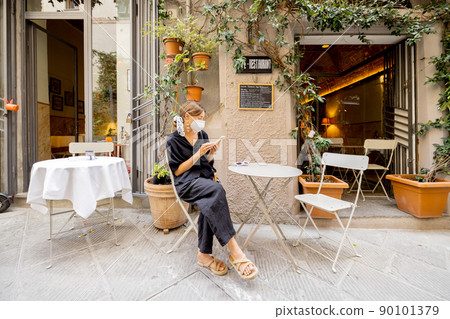 Woman in face mask sitting at italian restaurant outdoors Woman in face mask sitting at italian restaurant outdoors 90101379