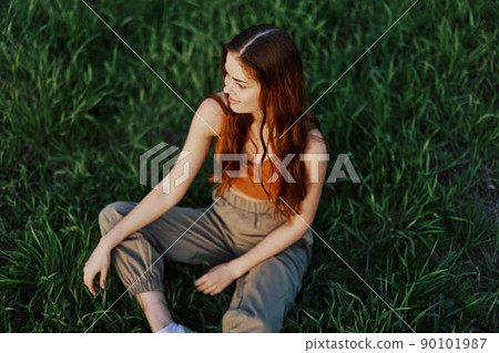 Freelance woman sitting in a park in summer on the grass looking at the sunset, sunshine in nature Freelance woman sitting in a park in summer on the grass looking at the sunset, sunshine in nature 90101987