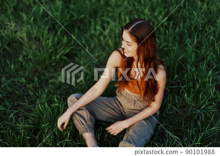 Freelance woman sitting in a park in summer on the grass looking at the sunset, sunshine in nature 90101988
