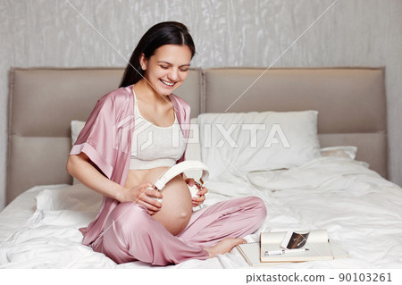 pregnant woman holding headphones on her belly 90103261