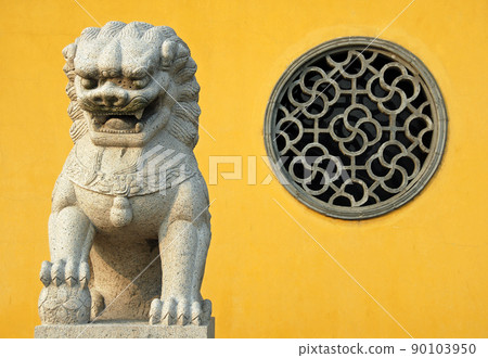 Zhenjiang, Jiangsu Province, China: A traditional Chinese lion statue against a yellow background and circular window at Dinghui Temple in Zhenjiang. 90103950