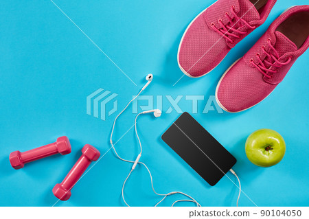 Flat lay shot of Sport equipment. Sneakers, dumbbells, earphones and phone on blue background. Flat lay shot of Sport equipment. Sneakers, dumbbells, earphones and phone on blue background. 90104050