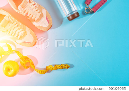 Sneakers with measuring tape on cyan blue background. Centimeter in yellow color near white trainers, close up. Sun flare Sneakers with measuring tape on cyan blue background. Centimeter in yellow color near white trainers, close up. Sun flare 90104065