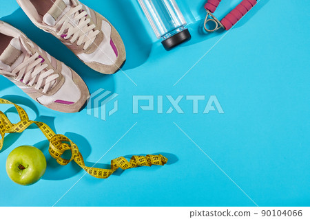 Sneakers with measuring tape on cyan blue background. Centimeter in yellow color near white trainers, close up. 90104066