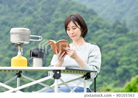 A woman reading a book while drinking coffee outdoors A woman reading a book while drinking coffee outdoors 90105563
