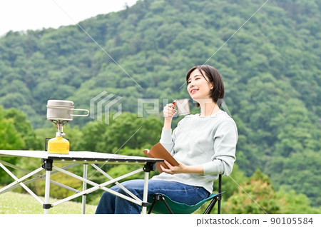 A woman reading a book while drinking coffee outdoors 90105584