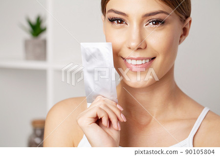Teeth whitening, beautiful smiling woman holding a whitening strip. 90105804