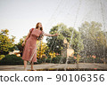 Young beautiful red-haired long-haired woman in a summer pink dress walks through the streets of a summer city. 90106356