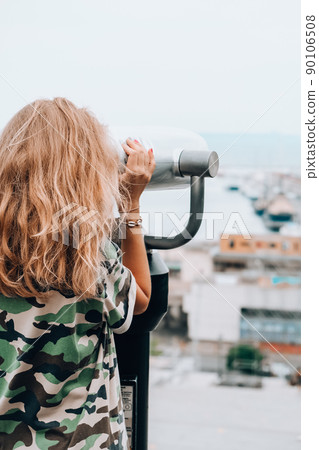 Woman looks through binoculars at the sea. Traveler vacation holiday concept. Using coin operated panoramic telescope 90106508