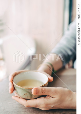 Women's hands hold a cup of tea at a table in a cafe. Women's hands hold a cup of tea at a table in a cafe. 90108328
