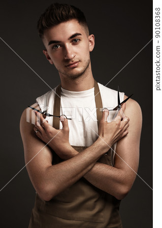 Handsome man hairdresser in a working uniform with scissors in his hands. Handsome man hairdresser in a working uniform with scissors in his hands. 90108368