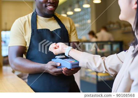 Close-up of woman using her smartwatch to pay online for order while waiter holding terminal Close-up of woman using her smartwatch to pay online for order while waiter holding terminal 90108568