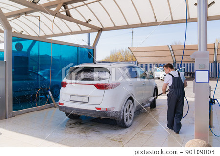 self-service car wash. a man in a work jumpsuit washes the car from a hose. self-service car wash. a man in a work jumpsuit washes the car from a hose. 90109003