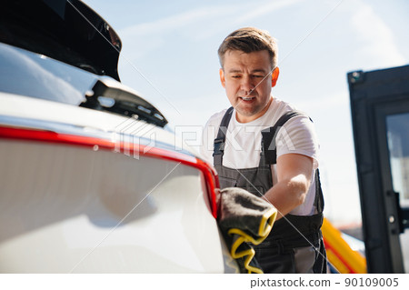 self-service car wash. a man in a work jumpsuit wipes the car dry after washing self-service car wash. a man in a work jumpsuit wipes the car dry after washing 90109005