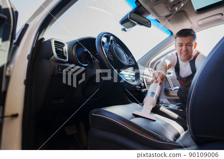 self-service car wash. man in work jumpsuit vacuuming car cabin after washing self-service car wash. man in work jumpsuit vacuuming car cabin after washing 90109006