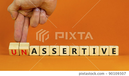Assertive or unassertive symbol. Businessman turns wooden cubes and changes concept words Unassertive to Assertive. Beautiful orange background. Business assertive or unassertive concept. Copy space. 90109307