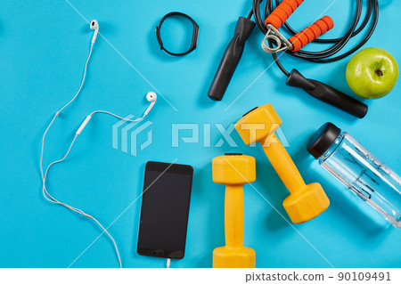 Dumbbells, mobile phone and skipping rope on blue background. Top view. Fitness, sport and healthy lifestyle concept. Dumbbells, mobile phone and skipping rope on blue background. Top view. Fitness, sport and healthy lifestyle concept. 90109491