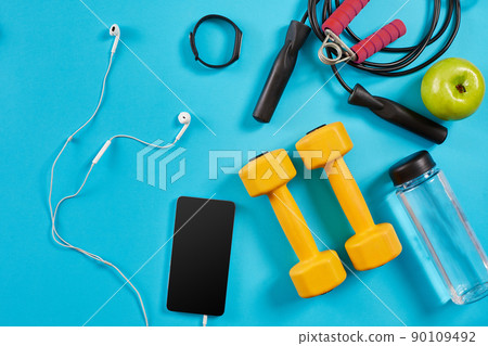 Dumbbells, mobile phone and skipping rope on blue background. Top view. Fitness, sport and healthy lifestyle concept. Dumbbells, mobile phone and skipping rope on blue background. Top view. Fitness, sport and healthy lifestyle concept. 90109492