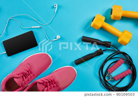 Flat lay shot of sneakers, jumping rope, dumbbells and smartphone on blue background. 90109503