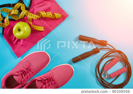 Flat lay of female sport equipments in pink color with jump rope and sneakers on blue background. Sun flare 90109508