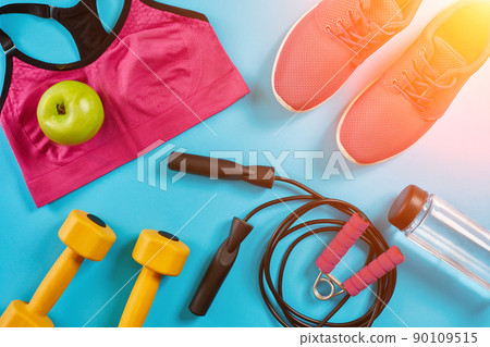 Athlete's set with female clothing, dumbbells and bottle of water on bright blue background. Sun flare 90109515