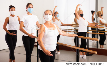 Women in masks exercising ballet moves in training room Women in masks exercising ballet moves in training room 90111845