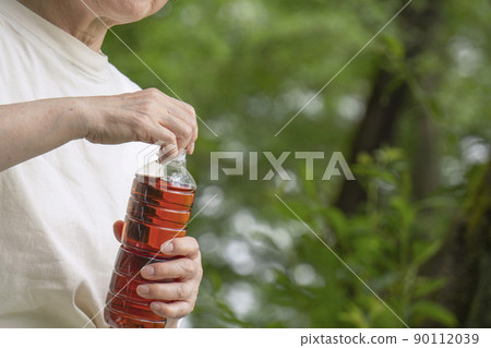 Senior woman drinking a bottle of drink in nature 90112039