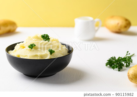 Mashed potato with parsley in black bowl on white and yellow background 90115982