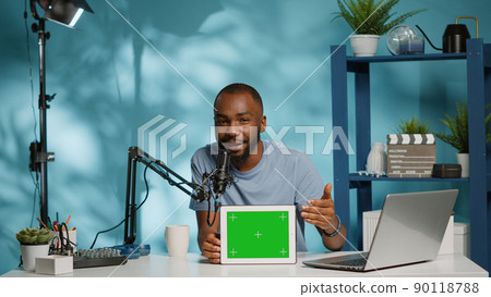 Black vlogger showing tablet with horizontal green screen on camera for podcast. African american man using chroma key with mockup template on digital gadget for vlog. Social media blogger 90118788