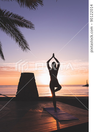 Young woman silhouette meditating in front of the beach at sunrise. Young woman silhouette meditating in front of the beach at sunrise. 90122014