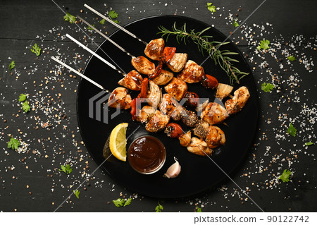 Plate with grilled chicken meat skewers and barbecue sauce on black rustic wooden table 90122742
