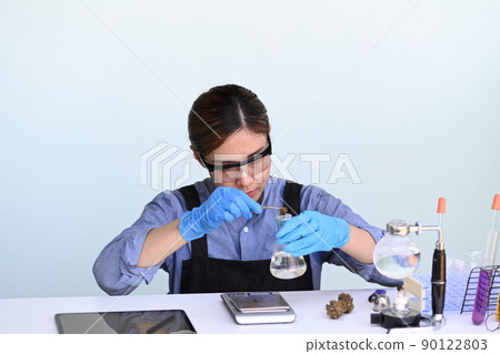 Scientist holding a glass bowl with cbd oil extracted from a marijuana plant during conducting scientific research in science lab. 90122803