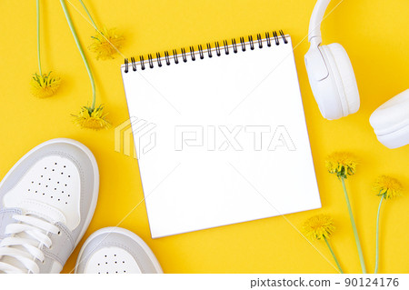 Summer template with white blank notebook, sneakers, headphones and flowers on a yellow background. Mock up in flat style. Top view Summer template with white blank notebook, sneakers, headphones and flowers on a yellow background. Mock up in flat style. Top view 90124176
