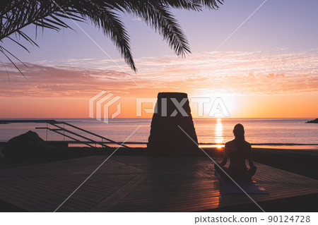 Young woman silhouette meditating at sunrise in front of the beach. Young woman silhouette meditating at sunrise in front of the beach. 90124728