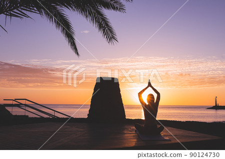 Young woman silhouette meditating in front of the beach at sunrise. Young woman silhouette meditating in front of the beach at sunrise. 90124730