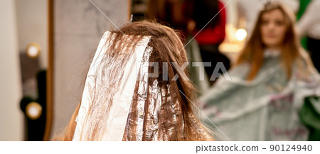 Beautiful young caucasian woman with foil in her hair while dyeing her hair sitting in a beauty salon 90124940