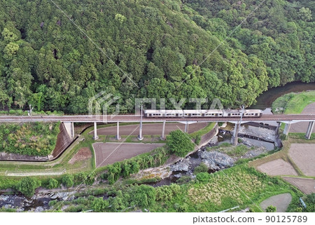 Sasaguri Line train running on the bridge with the fresh green in the background 90125789