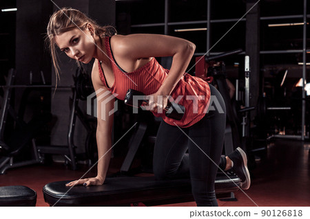 Young beautiful blonde girl is engaged in sports training with dumbbells in the gym 90126818