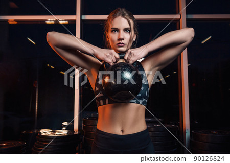 Attractive young athlete with muscular body exercising crossfit. Woman in sportswear doing crossfit workout with kettle bell at the gym Attractive young athlete with muscular body exercising crossfit. Woman in sportswear doing crossfit workout with kettle bell at the gym 90126824