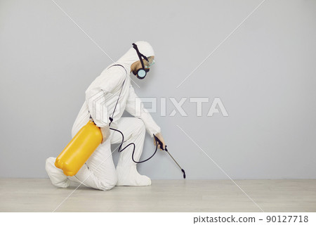 Pest control worker in protective suit spraying insecticide to clean house from insects 90127718