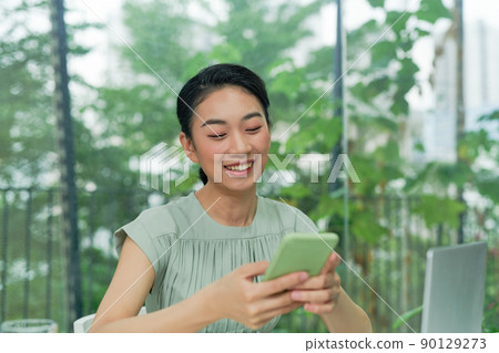Happy young elegant businesswoman scrolling in smartphone while enjoying break by workplace 90129273