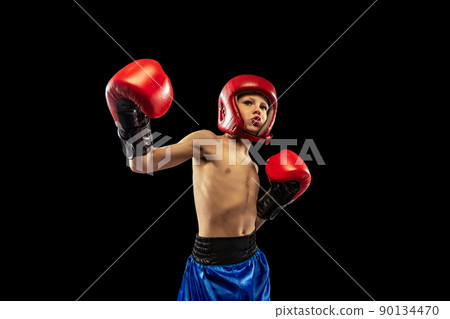 Dynamic portrait of sportive boy, kid in boxer gloves and shorts practicing isolated on dark background. Concept of sport, movement, studying, achievements, active lifestyle. 90134470