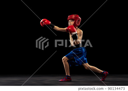 Dynamic portrait of sportive boy, kid in boxer gloves and shorts practicing isolated on dark background. Concept of sport, movement, studying, achievements, active lifestyle. Dynamic portrait of sportive boy, kid in boxer gloves and shorts practicing isolated on dark background. Concept of sport, movement, studying, achievements, active lifestyle. 90134473