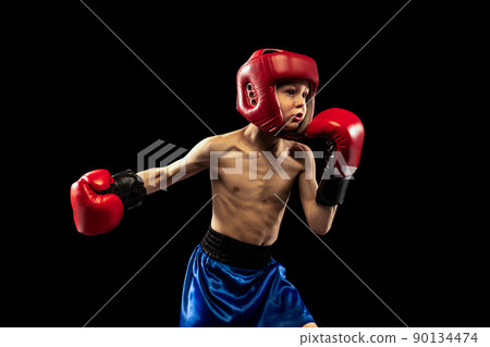 Dynamic portrait of sportive boy, kid in boxer gloves and shorts practicing isolated on dark background. Concept of sport, movement, studying, achievements, active lifestyle. Dynamic portrait of sportive boy, kid in boxer gloves and shorts practicing isolated on dark background. Concept of sport, movement, studying, achievements, active lifestyle. 90134474