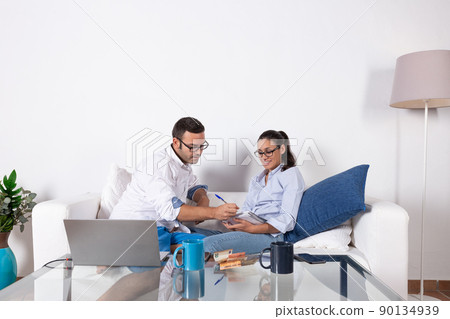 Young couple organizing their economy, taking notes on the couch in the living room at home, with laptop and money on the table. With copy space. 90134939